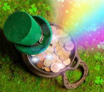 Leprechaun hat and horseshoe lie on green grass with rainbow and clover leaves and treasure pot