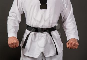Strong male athlete in a white kimono for taekwondo stands in a black belt sensei