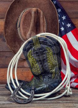 Shabby old ornate classic cowboy boots hat and lasso on wooden background and USA flag background