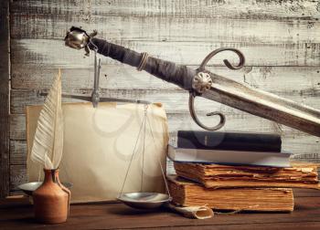 still life with the legendary attributes of justice scales and the sword of Themis, as well as old manuscripts and the Bible for taking the oath