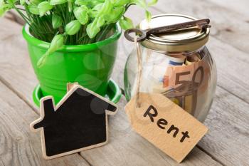Rental payment concept - money jar, key with label and little house on the wooden desk