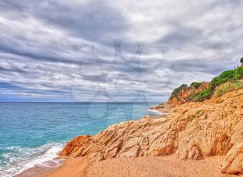HDR shot of the beach with clear Mediterranean Sea and rock on the coast.