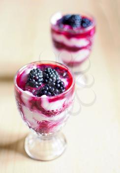 Glass cups with cream cheese blackberry desserts. Fresh blackberries are placed on top of the desserts.