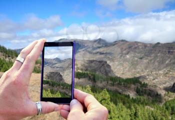 View over the mobile phone display during shooting Gran Canaria mountains. Holding the mobile phone in hands and taking a photo, focused on mobile phone screen.