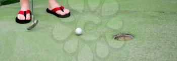 Playing mini golf. Low angle closeup view of mini golf ball and golf club near hole.