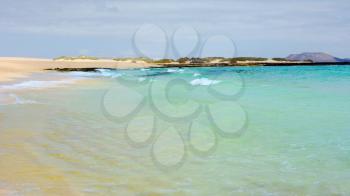 View of an empty Beach named Glass Beach with turquoise water and waves, near Corralejo town and natural dunes park on Fuerteventura island.