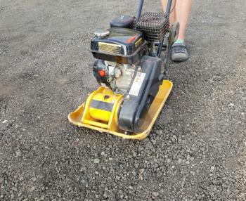 Worker is using vibrating plate compactor for ground road compaction.