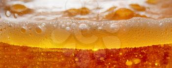 Closeup of illuminated beer with lot of bubbles and foam.