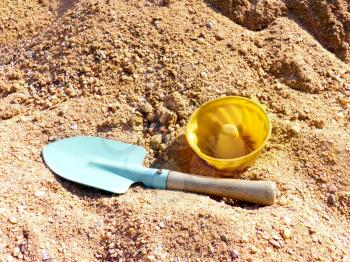 Close up of toy shovel and plastic cake on the sandbox sand.