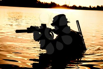 Silhouette of special forces with rifle in action during raid crossing river in the jungle waist deep in the water