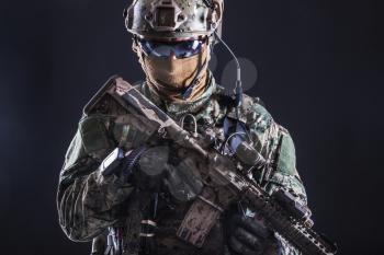 Half length studio shot of special forces soldier in field uniforms with weapons, portrait on black background. Protective goggles glasses are on