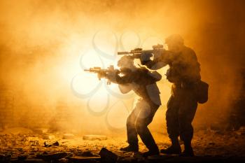 Black silhouettes of pair of soldiers in the smoke fire burning moving in battle operation. Back light