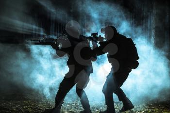 Black silhouettes of pair of soldiers in the smoke moving in battle operation. Back light