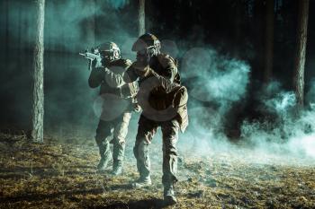 Image of soldiers in the smoke moving in battle operation. Back light, dark night, forest
