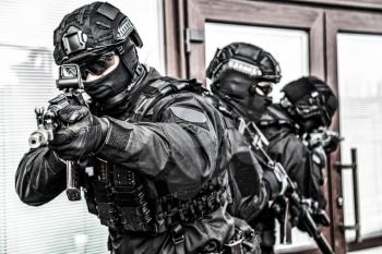 Police special operations immediate reaction team members in blank black uniform, tactical ammunition and mask, armed with assault rifle covering each other during hostage rescue or security operation