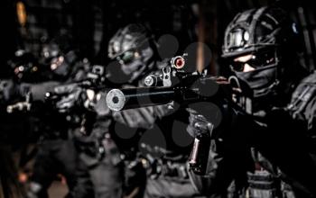 Police special operations, quick reaction tactical group members in black uniforms, helmet and hidden behind masks faces standing in line, aiming with assault rifles on terrorism response operation