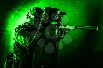 Police special operations team, quick response group fighter in black uniform, helmet and mask aiming with pistol equipped silencer while hiding behind ballistic shield, toned, low key studio shoot