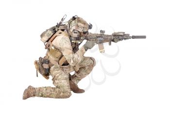 Modern army infantry soldier in combat uniform and helmet standing on knee, aiming with laser sight on service rifle, shooting in enemy during firefight studio shoot isolated on white background