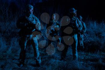 Army special operations tactical group, military saboteurs team armed fighters standing in grassy area at nighttime, hiding faces behind masks, moving silently in darkness, patrolling area at nigh
