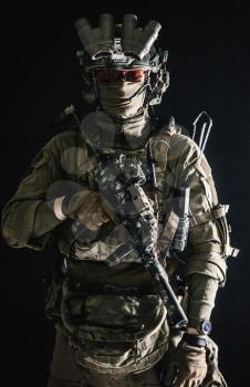 Anti-terrorist squad fighter, army elite forces soldier in combat uniform and tactical ammunition, armed mini submachine gun, wearing night-vision device, low key studio portrait on black background