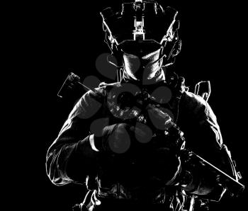 Modern infantry soldier, special operations forces tactical group shooter armed submachine gun with silencer, equipped radio headset and quad-tube night vision device standing in darkness, desaturated