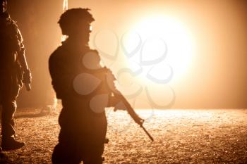 Black silhouette of soldier at night. Back light, cropped, toned and colorized