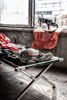 Stationary fire position, outpost observation post in abandoned building with machine gun standing on bipod in window, tactical helmet, sleeping bag and U.S. Marine Corps flag lying on military cot