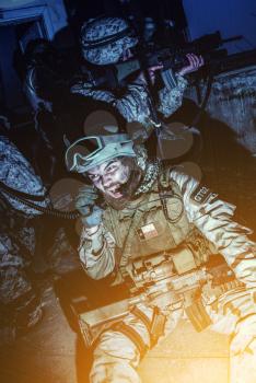 Commando team leader, counter terrorist squad officer, military operator screaming in radio handset while calling for reinforcements, evacuation or artillery support during intensive night firefight