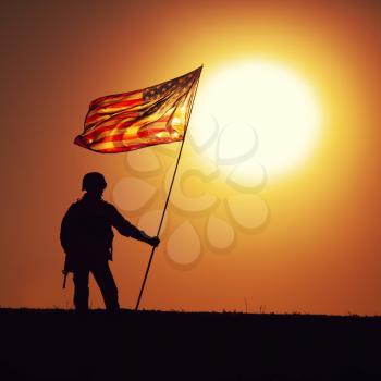 Silhouette of US army infantry soldier, United States Marines Corps fighter standing on sunset horizon with waving USA national flag. Soldiers heroism and victory in battle, honoring of fallen heroes