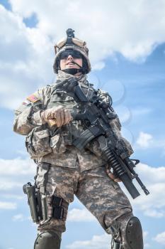Portrait of United states airborne infantry corporal with arms, camo uniforms dress. Combat helmet on, half lengh portrait, low angle