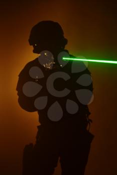 Studio shot of swat police operator with laser sights on rifle. Fire smoke screen background. Laser rays beams