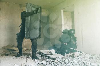 Team squad of swat police special forces in action hiding behind ballistic shield ruined building. One operator is injured wounded