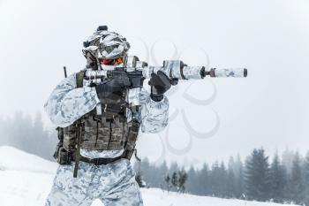 Winter arctic mountains warfare. Action in cold conditions. Trooper with weapons in forest somewhere above the Arctic Circle