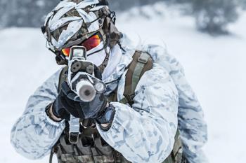 Winter arctic mountains warfare. Action in cold conditions. Trooper with weapons in forest somewhere above the Arctic Circle, pointing at camera