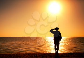 Silhouette of saluting commando soldier, army infantryman standing on shore during sunset or sunrise. Military solemn ceremony, respectable salute for honoring fallen heroes and comrades veterans