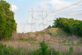 Electricity pylons and wires in a green field against blue sky