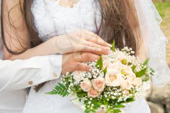 Hands of newlyweds with rings, against a wedding bouquet