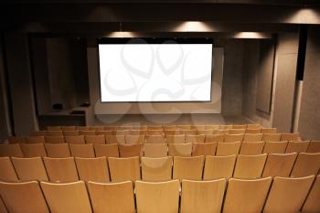 Empty cinema with white isolated screen and brown chairs.
