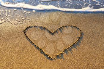Heart drawn on the beach sand with sea foam and wave 