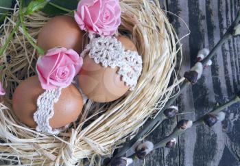 Nest with decorated eggs, roses and willow twigs on vintage wooden background. Spring Easter holiday arrangement.
