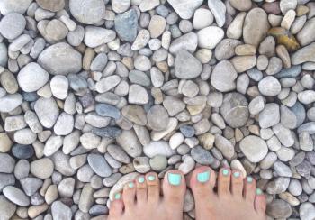Women's feet on the background of sea stones. Legs on a colorful sea pebbles.