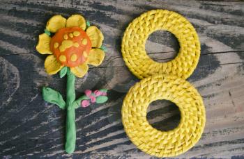 8 March symbol and handmade plasticine flower on wooden background. Happy woman's day design. Can be used as a decorative greeting card or postcard for international Woman's Day on 8 March.