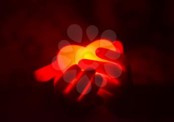 Human hands holding red glowing heart in the dark.