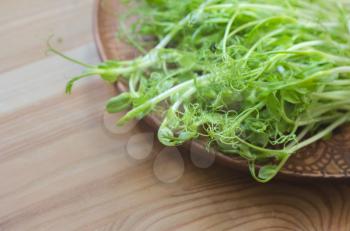 Seedlings of peas on an earthenware plate on a wooden background. Organic microgreens.