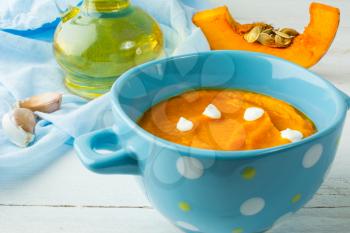 Creamy pumpkin squash vegetable soup with cream in a blue bowl on white wooden background