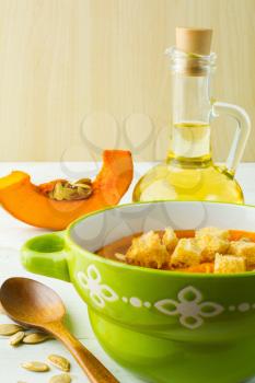 Pumpkin soup with croutons and pumpkin seeds in a green bowl on white wooden background, vertical