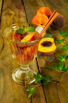 Refreshing drink, iced green tea with peaches and mint in a glass on a dark wooden background, vertical, selective focus