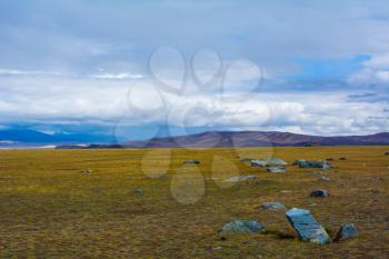 Steppe landscape with large stone in the foreground, mountains view, blue sky with clouds. Chuya Steppe, Kuray steppe in the Siberian Altai Mountains, Russia