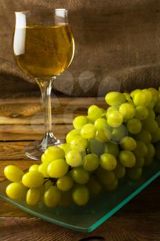Bunch of white grapes and a glass of wine on a dark wooden background. Cluster of grapes. Bunch of grapes. Cluster grapes.  Bunch grapes. Grapes. Grape. Glass of wine. Glass wine. Grape vine