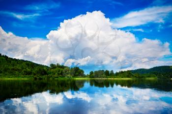 Beautiful landscape of the island and the blue sky with white clouds reflected in the clear water. Wooded shore of a mountain lake. Summer idyllic landscape.